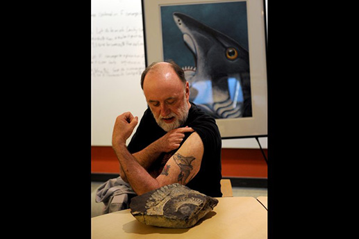 Ketchikan artist Ray Troll shows his ratfish tattoo next to the Helicprion fossil at the UAA ConocoPhillips Integrated Science building in Anchorage, AK on Wednesday, May 13, 2015. Barrow, AK geologist Richard Glenn found the buzz-tooth shark fossil Helicoprion on the North Slope when he was a student. The provenance of the fossil was lost when the Smithsonian miscategorized it. Troll was instrumental in having it found in the collection and getting Glenn credit for finding the only Helicprion fossil found in Alaska. The fossil will be on display at the Alaska SeaLife Center in Seward, AK this summer. Bob Hallinen / ADN